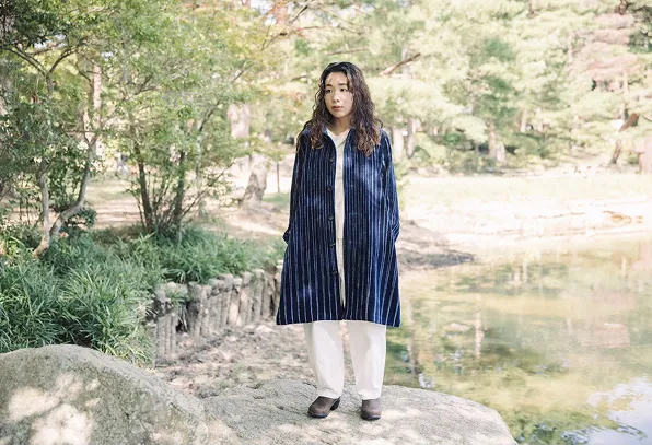 播州織のコートを着て池の辺りに立っている女性