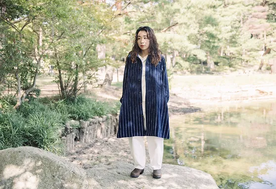 播州織のコートを着て池の辺りに立っている女性